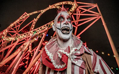 Clown in front of roller coaster at Knott's Berry Scary Farm, Southern California.