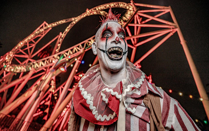 Clown in front of roller coaster at Knott's Berry Scary Farm, Southern California.