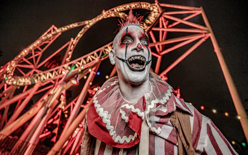 Clown in front of roller coaster at Knott's Berry Scary Farm, Southern California.