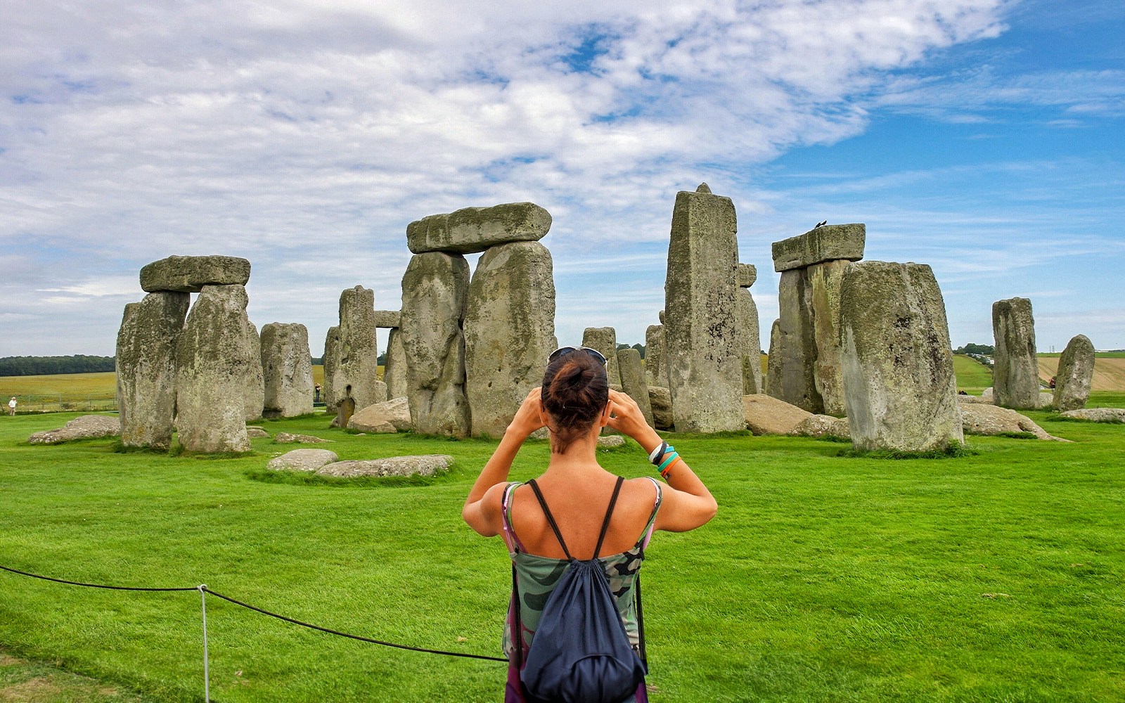 Visitor photographing Stonehenge with audio guide, Wiltshire, England.