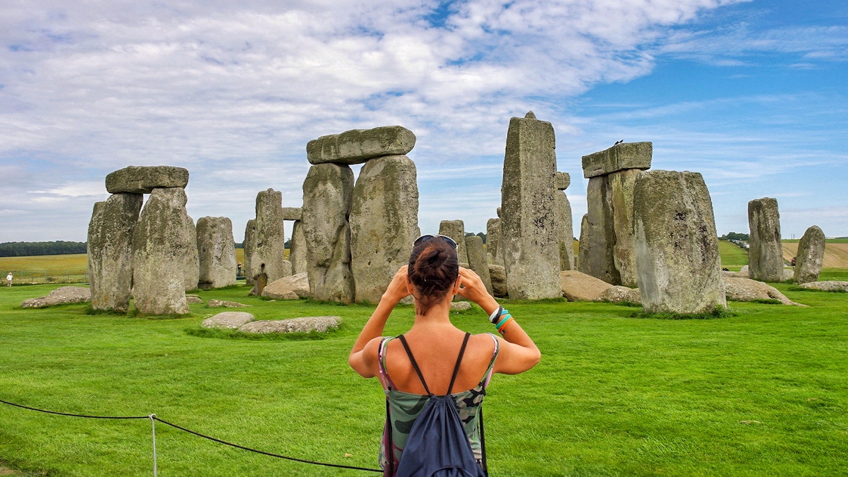 Visitor photographing Stonehenge with audio guide, Wiltshire, England.