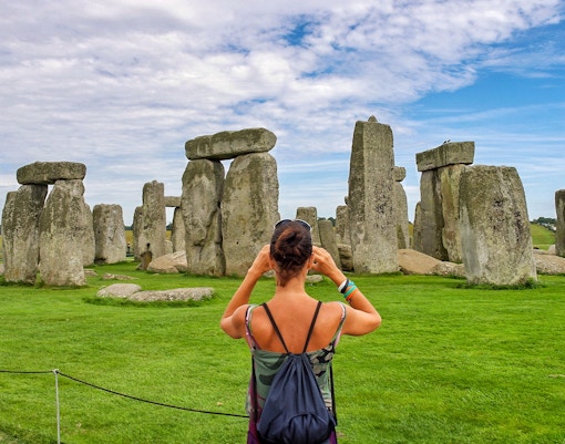 Visitor photographing Stonehenge with audio guide, Wiltshire, England.