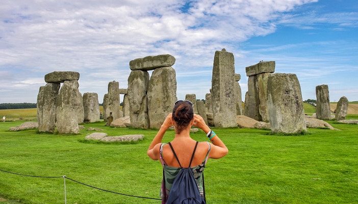 Visitor photographing Stonehenge with audio guide, Wiltshire, England.