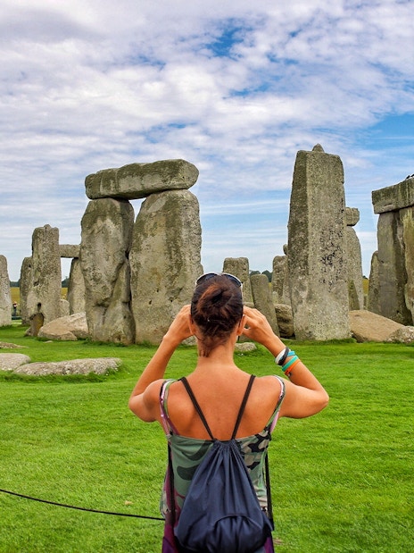 Visitor photographing Stonehenge with audio guide, Wiltshire, England.