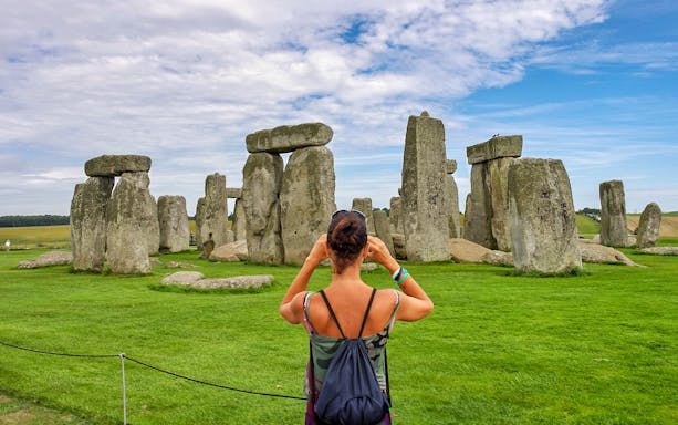 Visitor photographing Stonehenge with audio guide, Wiltshire, England.