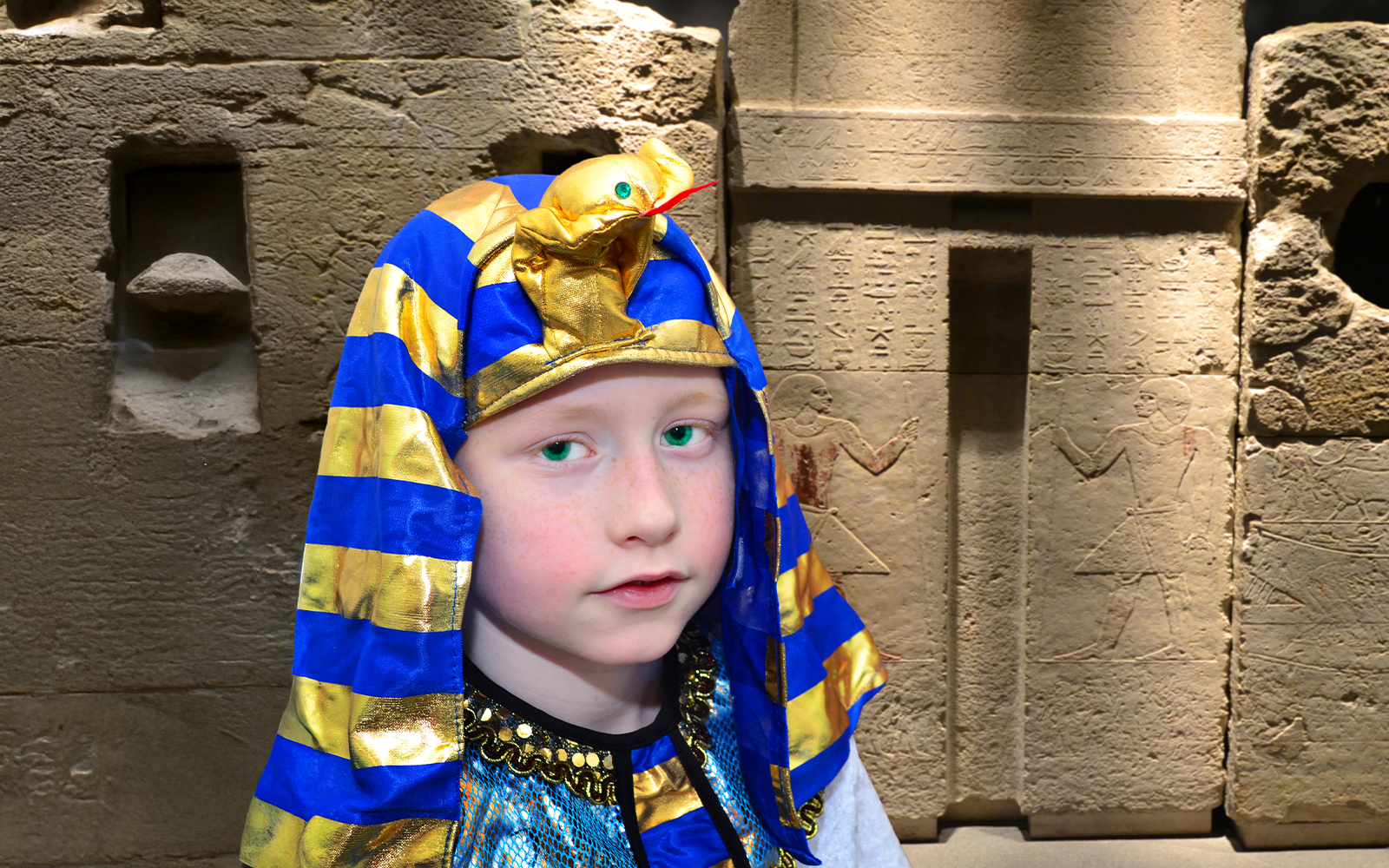 Child in pharaoh costume at Cairo Egyptian Museum with ancient hieroglyphs in background.