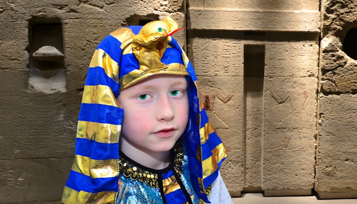 Child in pharaoh costume at Cairo Egyptian Museum with ancient hieroglyphs in background.