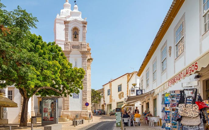 Historic street with bell tower and shops in Lagos, Western Algarve.