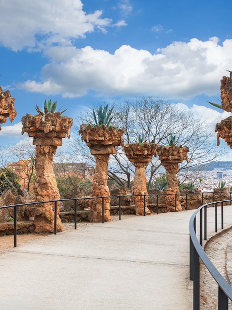 Stone columns with plants along a pathway in Park Güell, Barcelona.