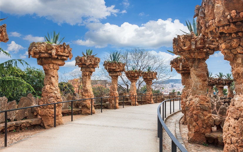 Stone columns with plants along a pathway in Park Güell, Barcelona.