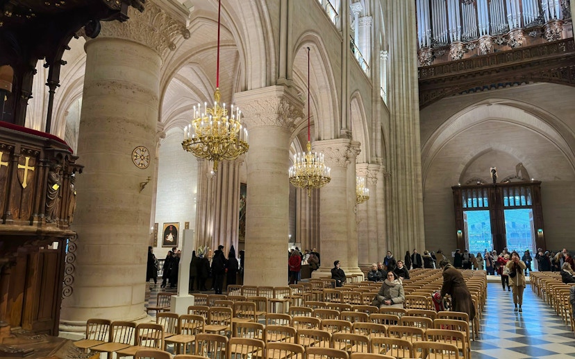 Notre Dame Cathedral interior with chandeliers and visitors seated in wooden chairs.