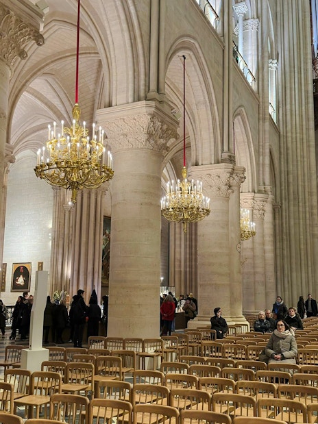 Notre Dame Cathedral interior with chandeliers and visitors seated in wooden chairs.