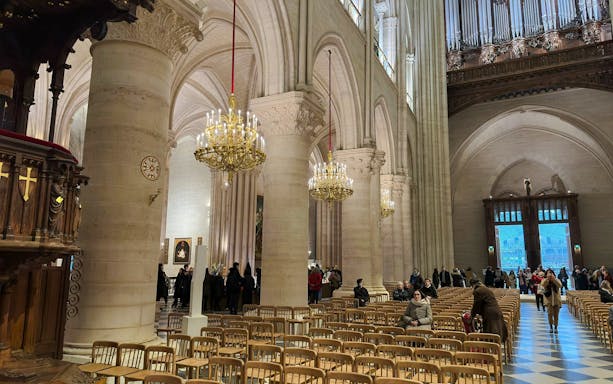 Notre Dame Cathedral interior with chandeliers and visitors seated in wooden chairs.