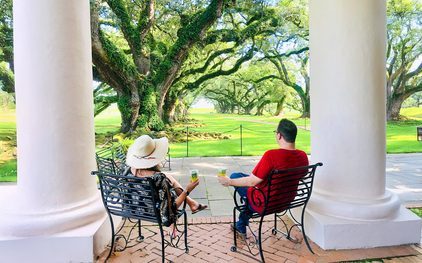 Visitors relaxing on a porch at Oak Alley Plantation, viewing the iconic oak trees.