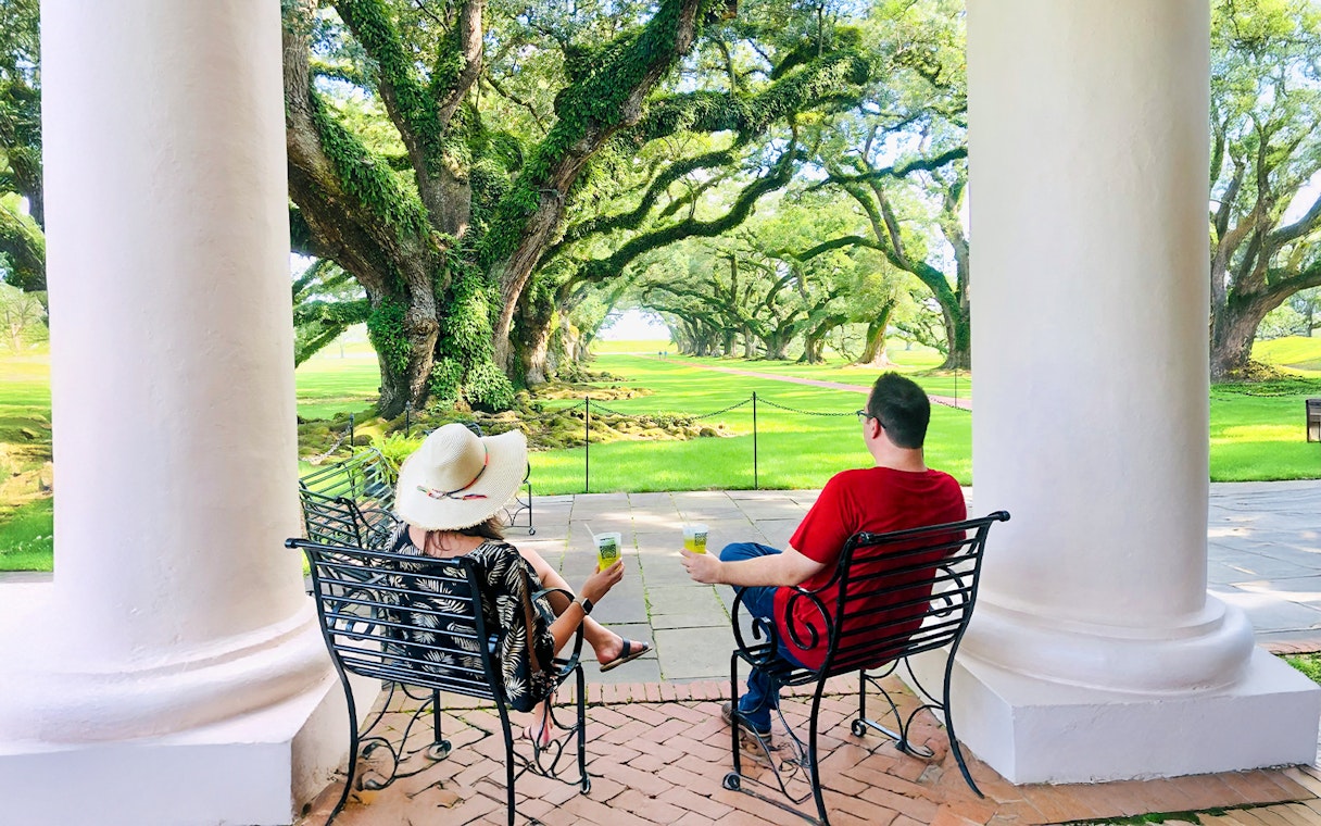 Visitors relaxing on a porch at Oak Alley Plantation, viewing the iconic oak trees.