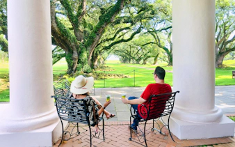 Visitors relaxing on a porch at Oak Alley Plantation, viewing the iconic oak trees.