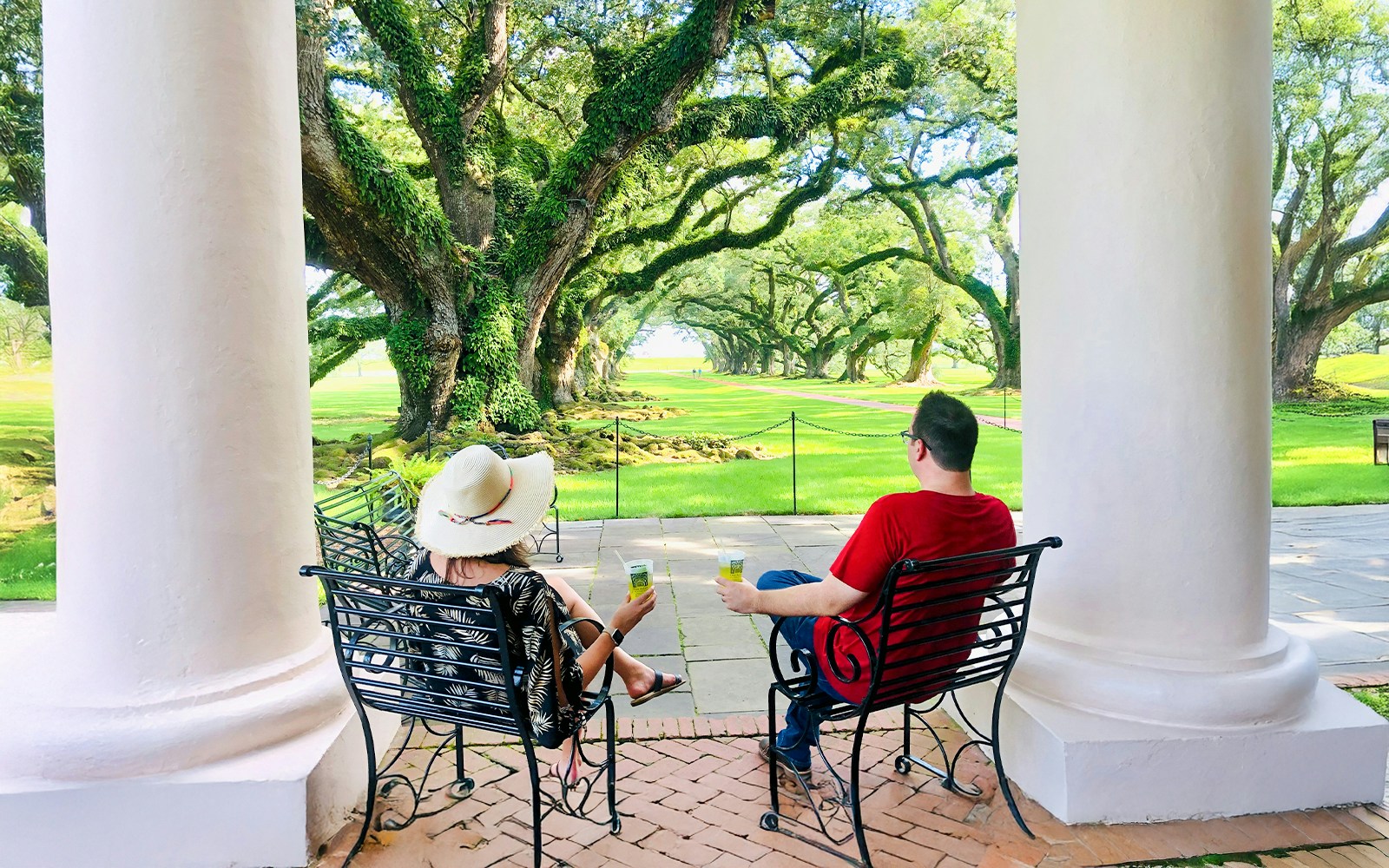 Visitors relaxing on a porch at Oak Alley Plantation, viewing the iconic oak trees.