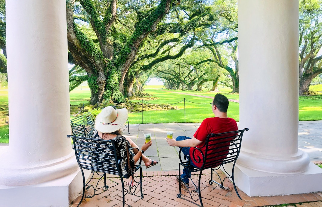 Visitors relaxing on a porch at Oak Alley Plantation, viewing the iconic oak trees.