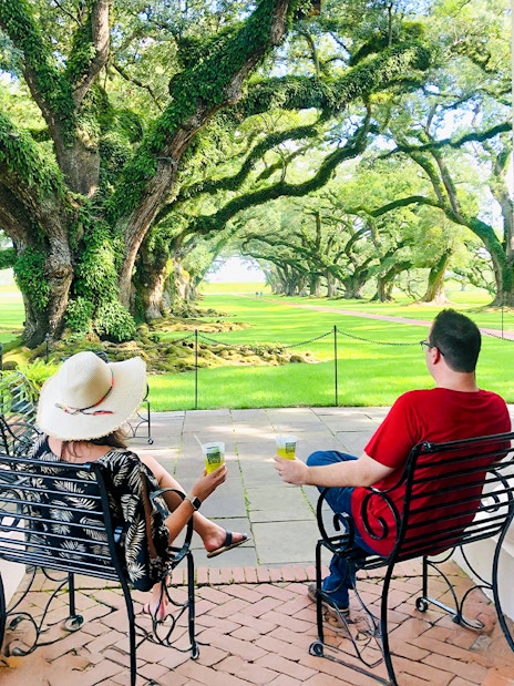 Visitors relaxing on a porch at Oak Alley Plantation, viewing the iconic oak trees.