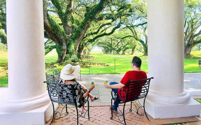 Visitors relaxing on a porch at Oak Alley Plantation, viewing the iconic oak trees.