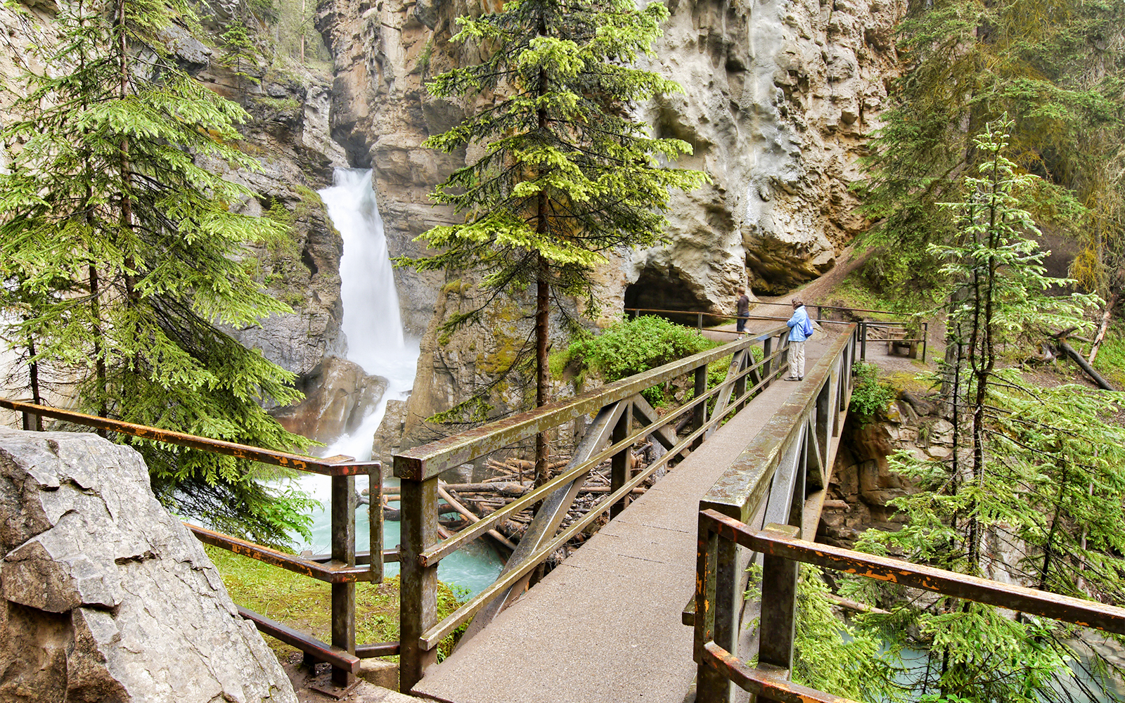 Bridge leading to Johnston Canyon falls in Banff National Park, Canada, surrounded by trees and rocky cliffs.