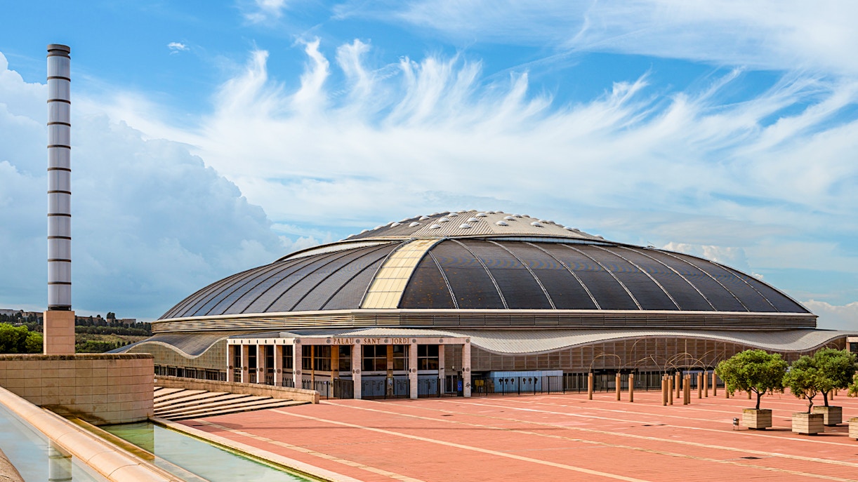 Palau Sant Jordi Barcelona exterior with iconic arched roof and surrounding greenery.