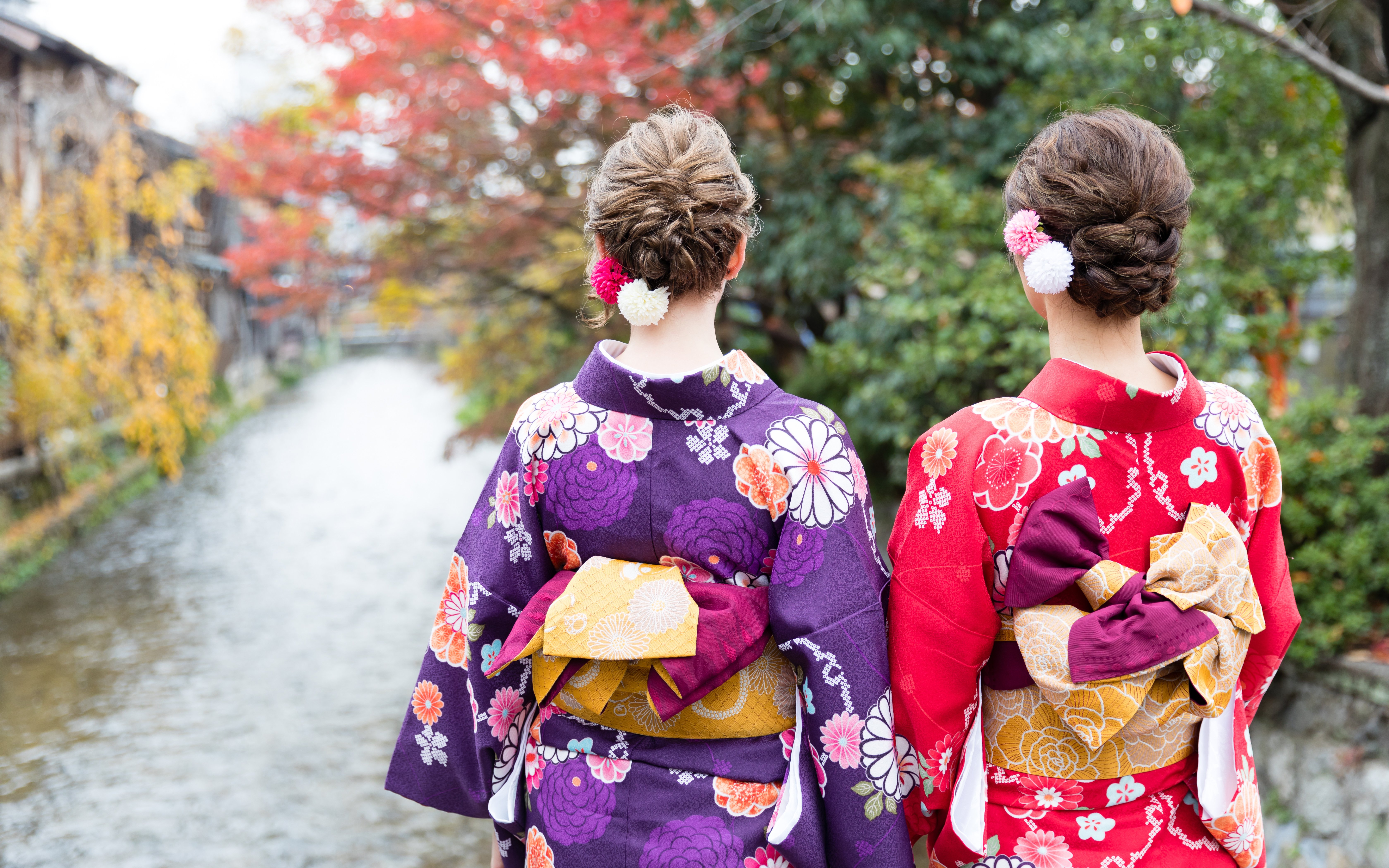 Women in colorful kimonos by a river in Kyoto during autumn.