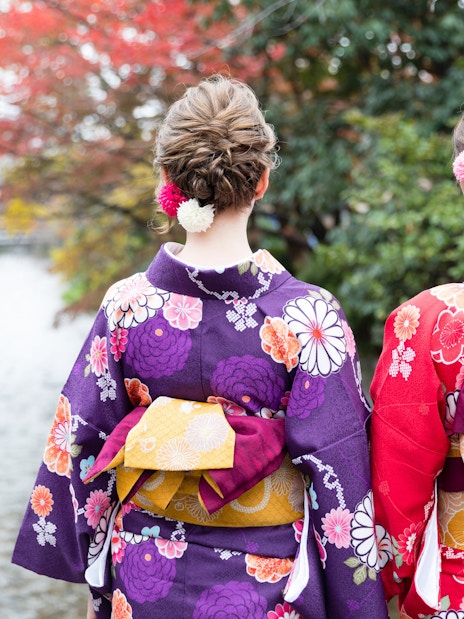 Women in colorful kimonos by a river in Kyoto during autumn.