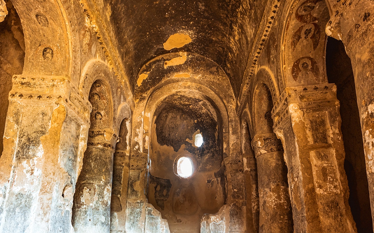 Ancient rock-cut church interior in Ihlara Valley, Cappadocia, with arched ceilings and faded frescoes.