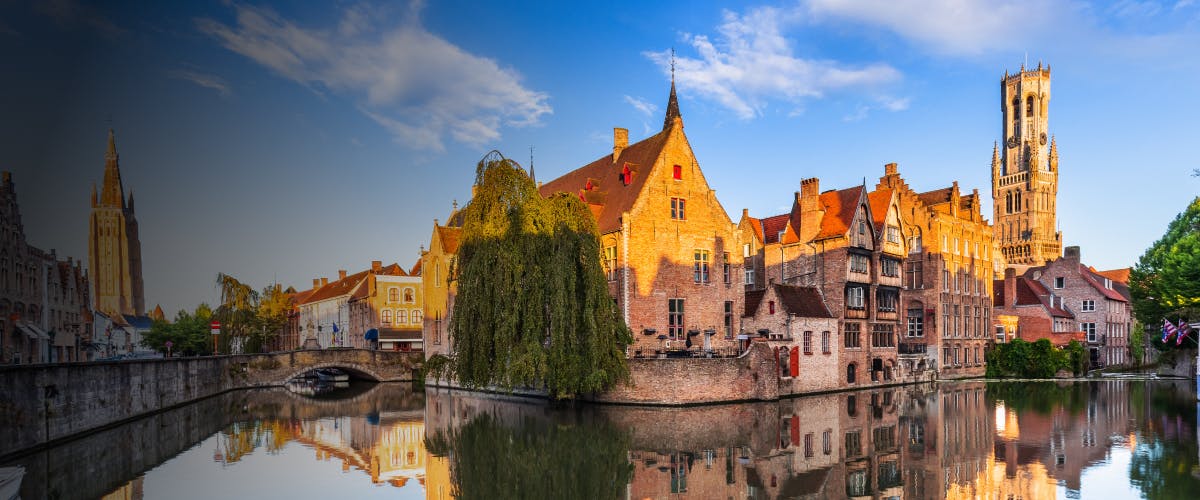 Canal view with historic buildings and Belfry tower in Bruges, Belgium.