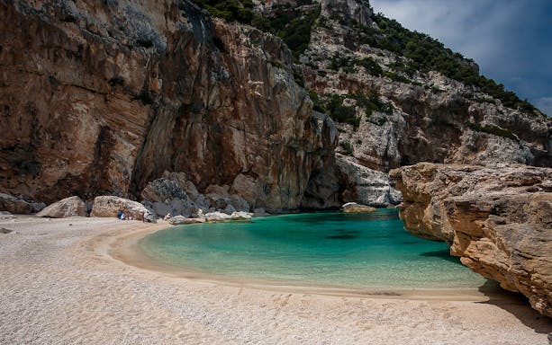 Cala Mariolu beach with turquoise water and rocky cliffs, ideal for trekking.