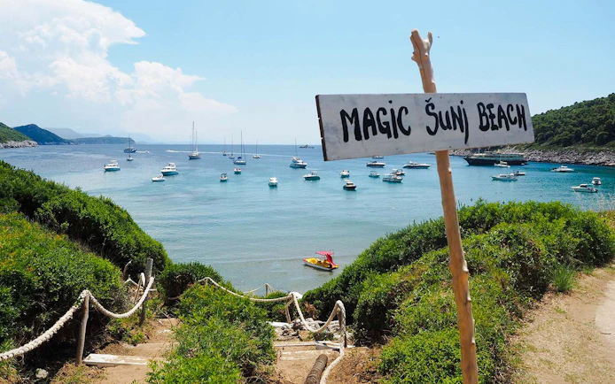Pathway leading to Šunj Beach with boats anchored in the bay, Lopud Island, Croatia.