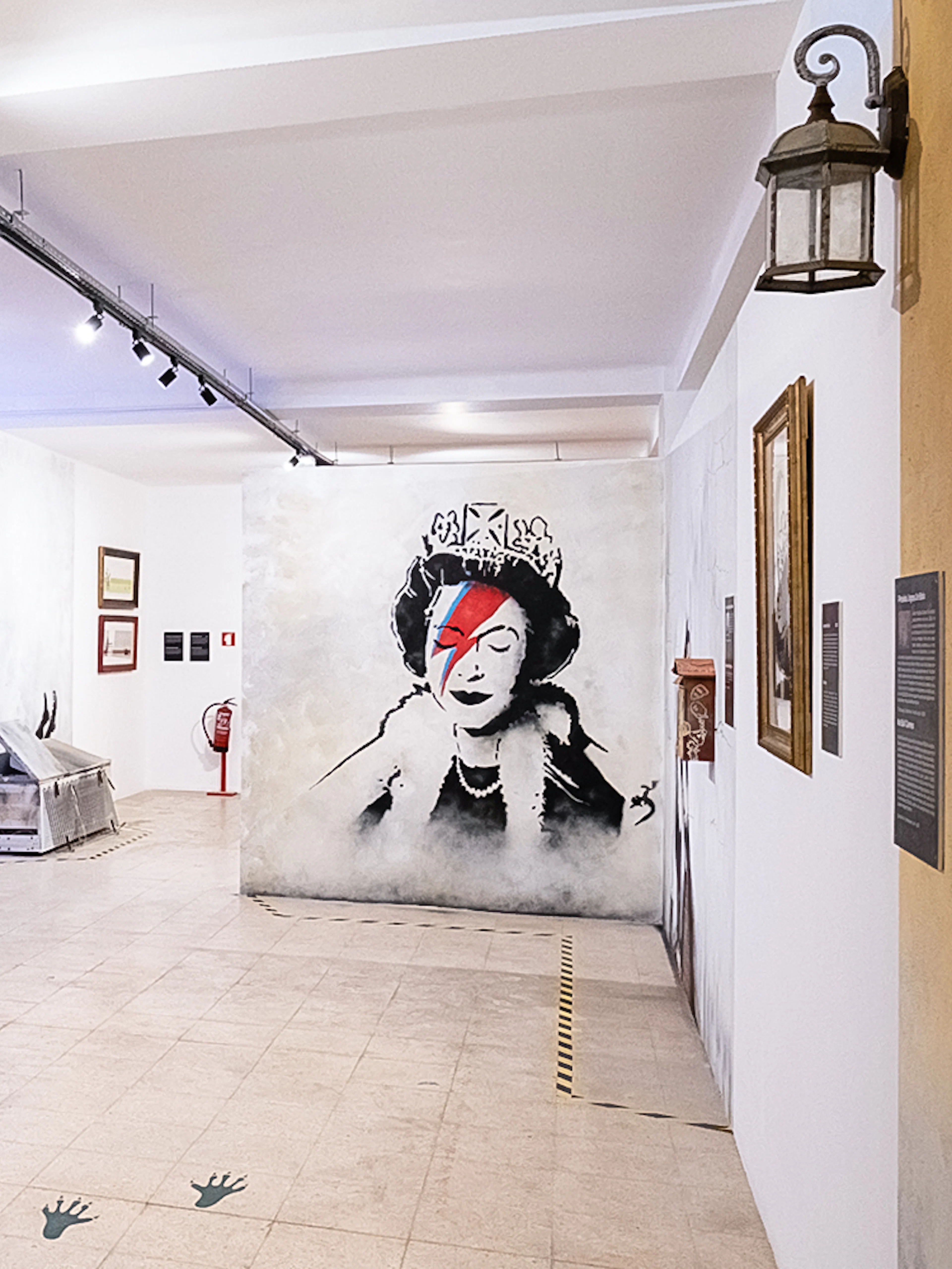 Banksy artwork in Lisbon museum featuring child with sewing machine and queen portrait.