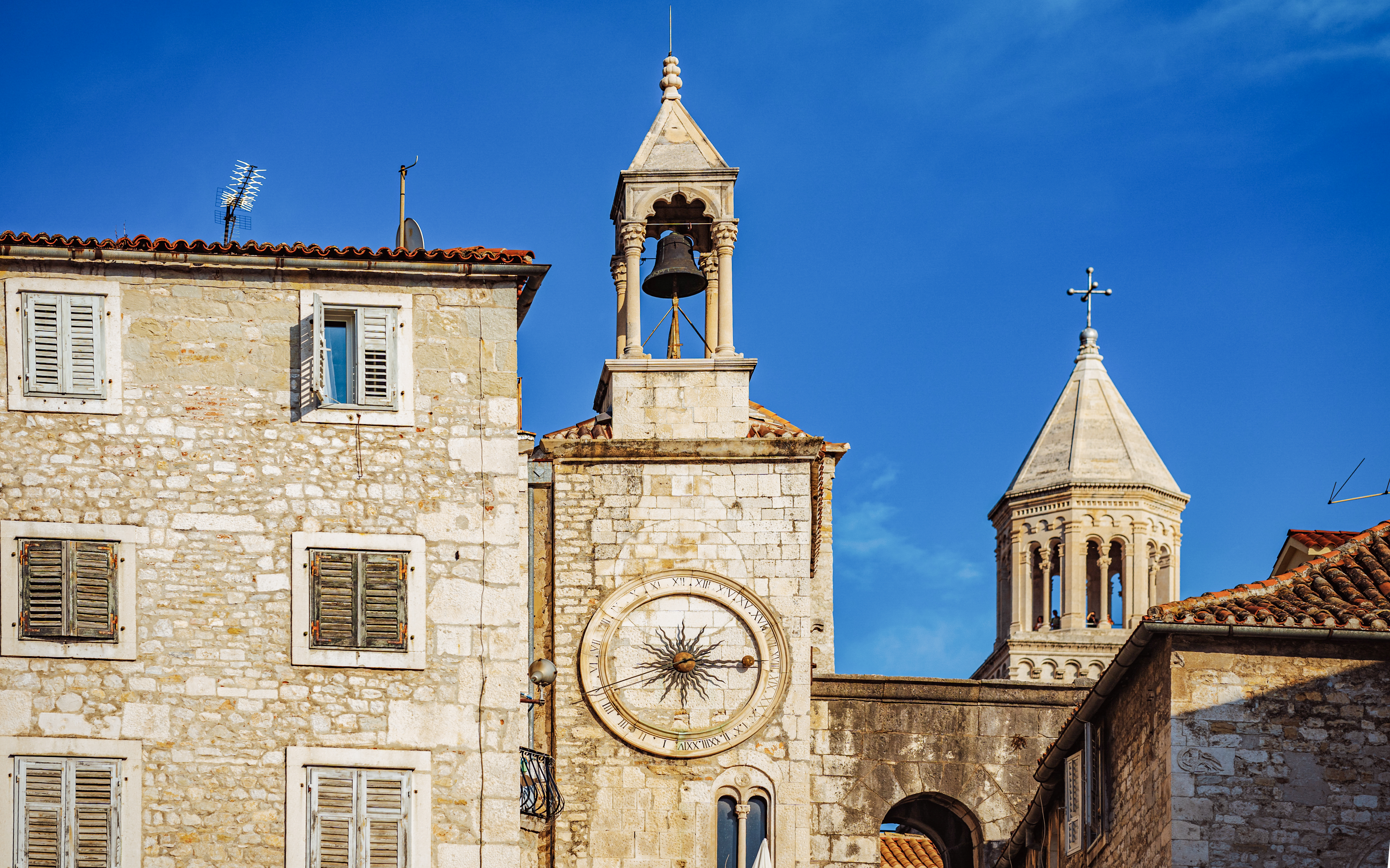 Clocktower and bell in Split, Croatia, with stone buildings and clear blue sky.