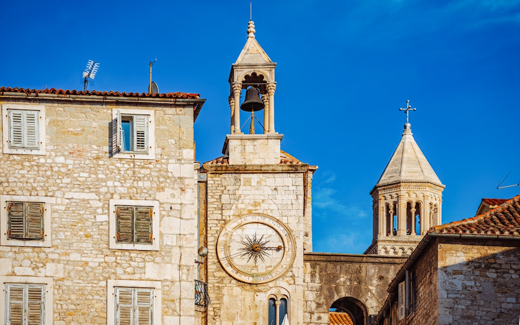 Clocktower and bell in Split, Croatia, with stone buildings and clear blue sky.