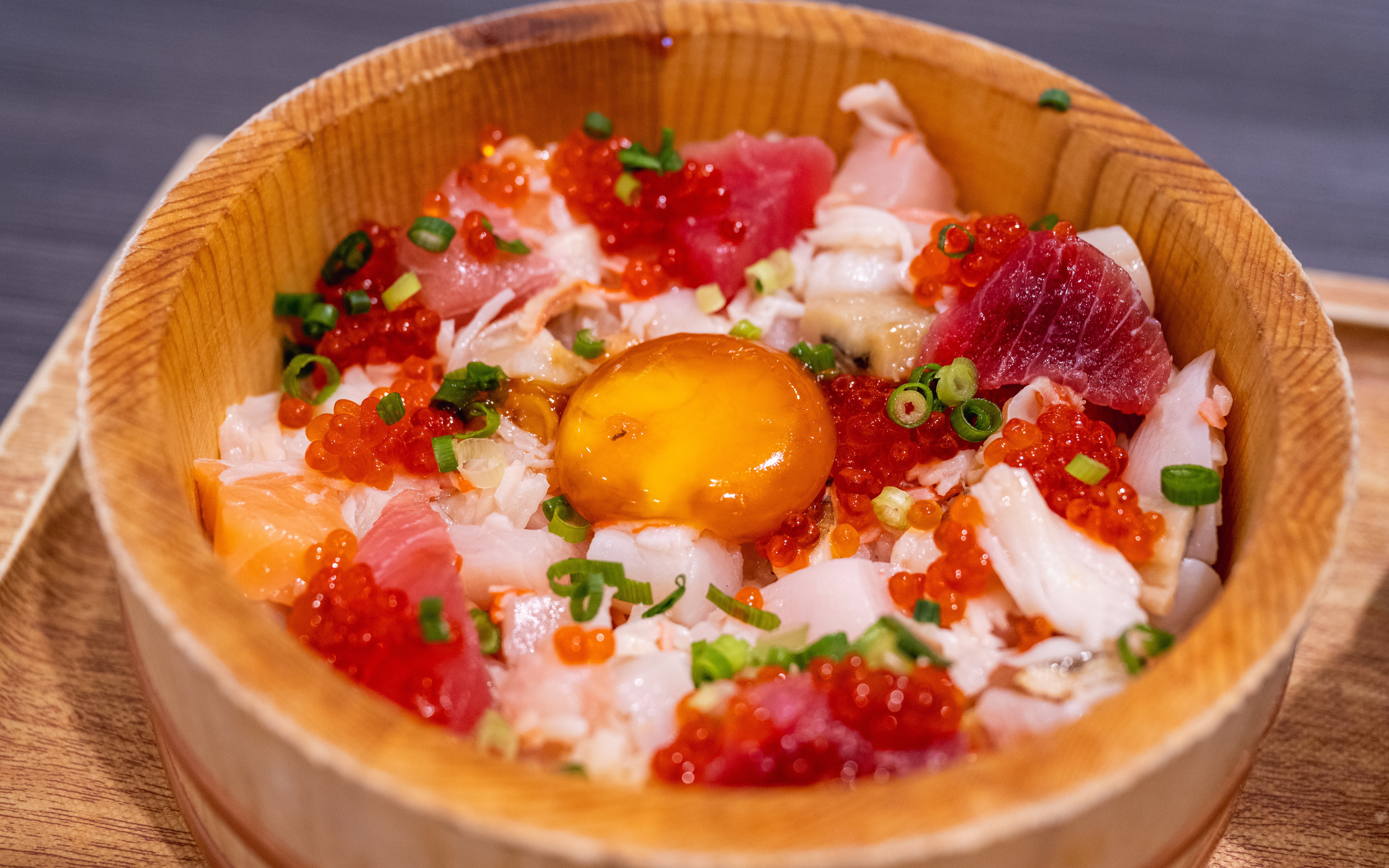 Japanese sashimi bowl with assorted fish, roe, and egg yolk in a wooden dish.