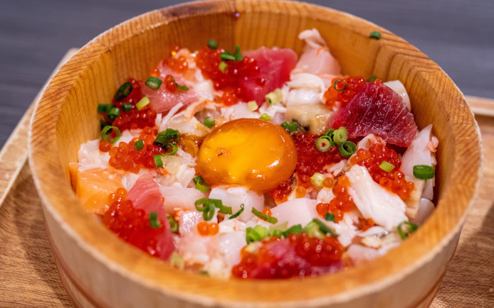 Japanese sashimi bowl with assorted fish, roe, and egg yolk in a wooden dish.