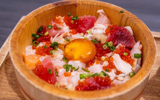 Japanese sashimi bowl with assorted fish, roe, and egg yolk in a wooden dish.