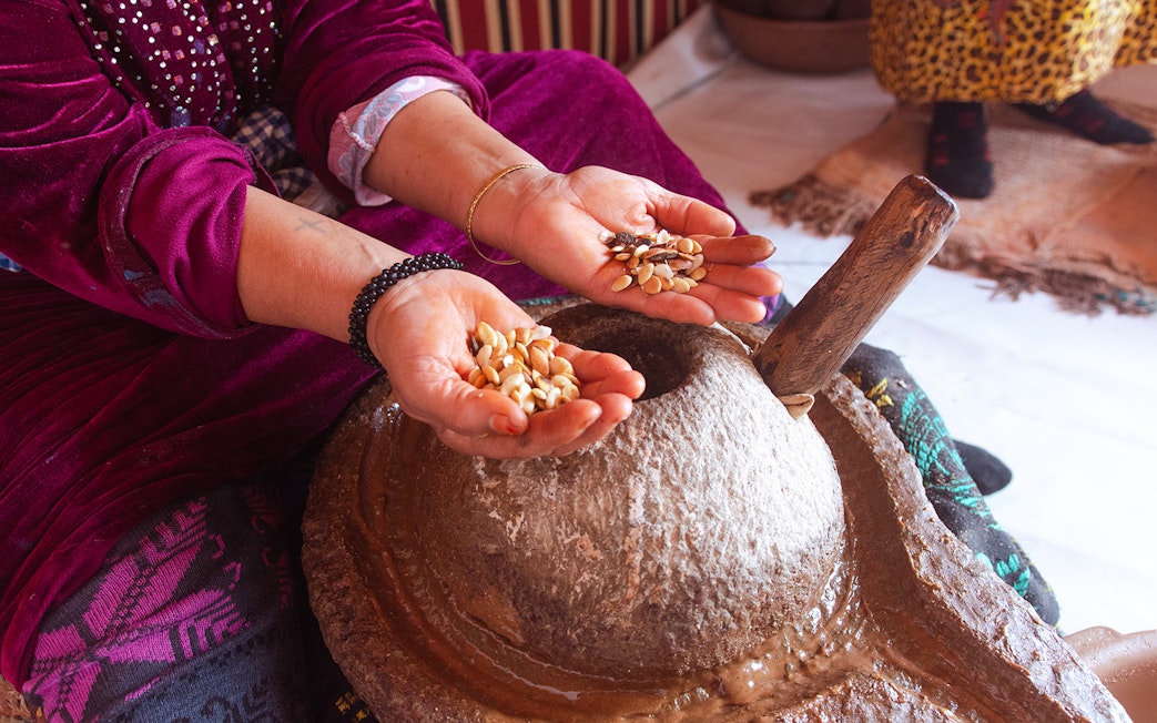 Hands holding argan nuts over a traditional stone grinder in Essaouira.
