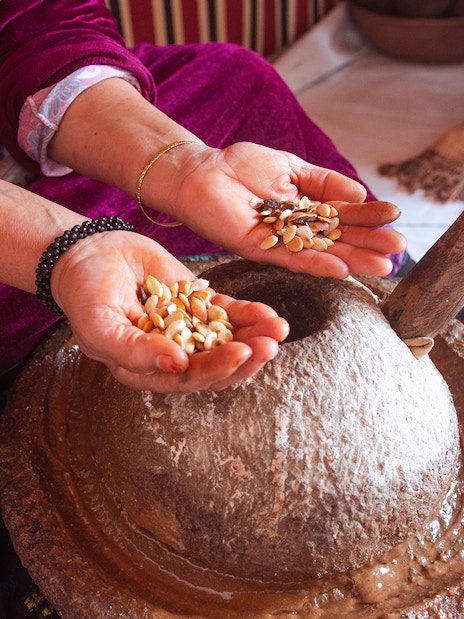 Hands holding argan nuts over a traditional stone grinder in Essaouira.