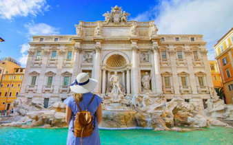 Visitor admiring Trevi Fountain in Rome with clear blue sky.
