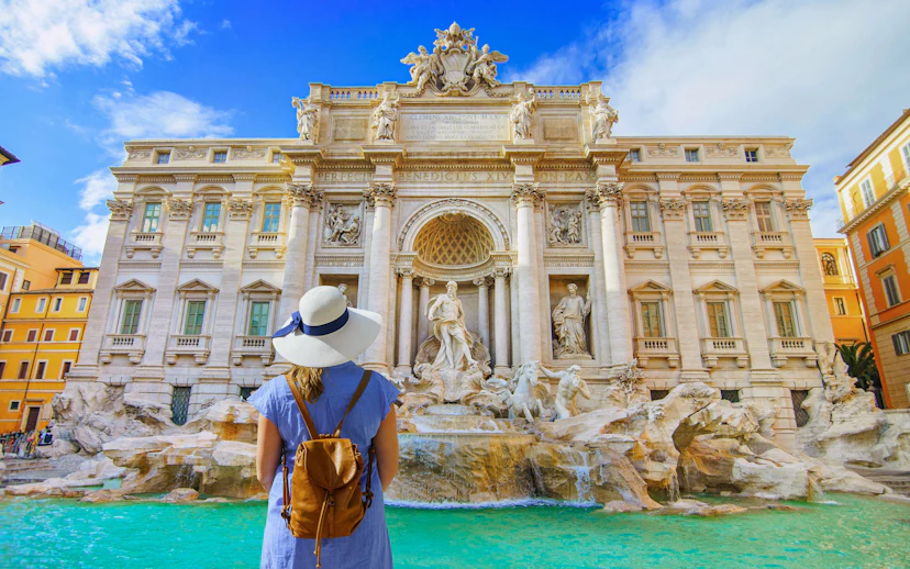 Visitor admiring Trevi Fountain in Rome with clear blue sky.