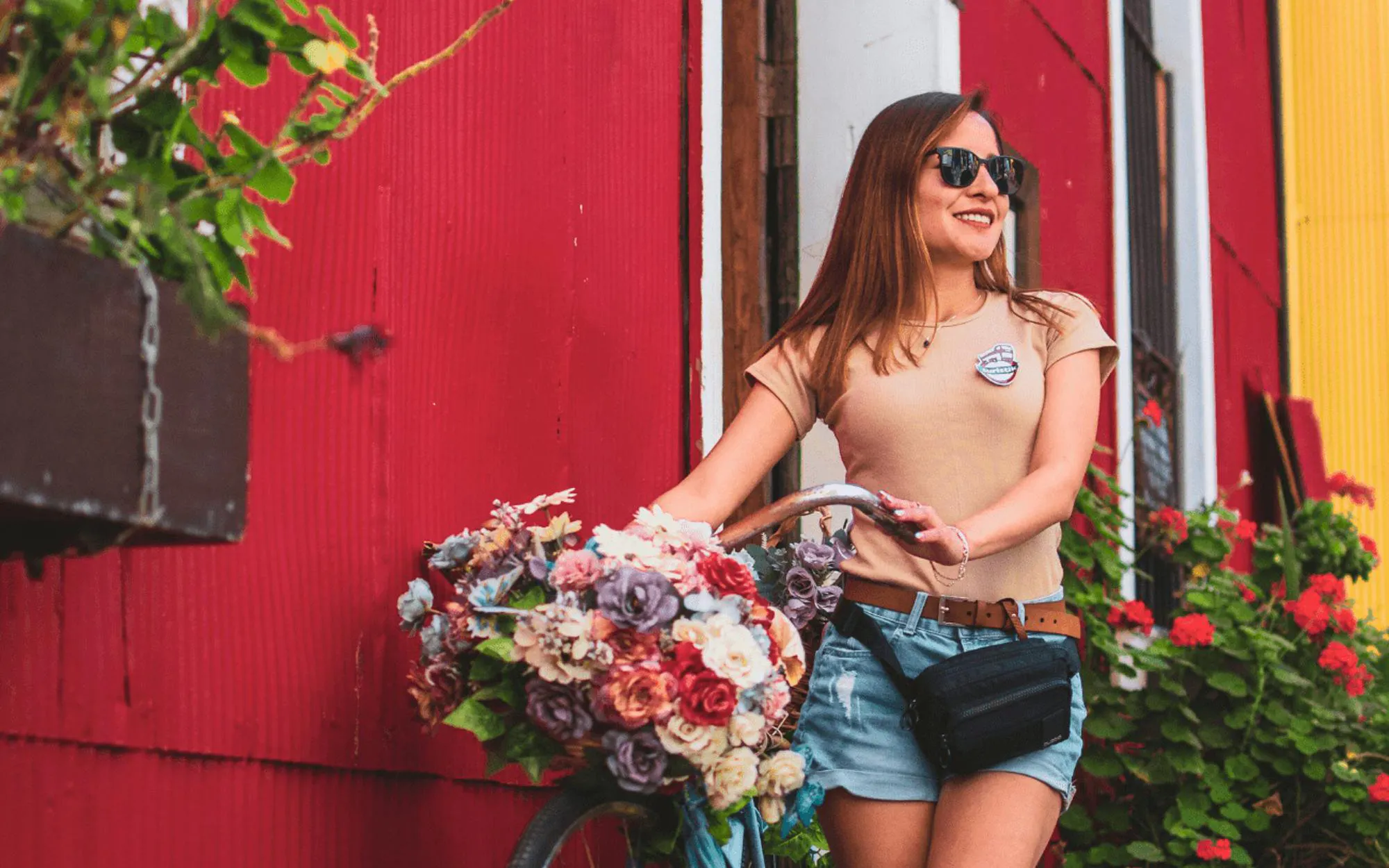 Woman with bicycle and flower basket in front of colorful building.
