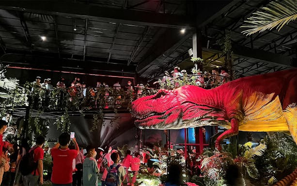 Visitors exploring Dinosaur Encounter World in Perak with a large dinosaur exhibit.