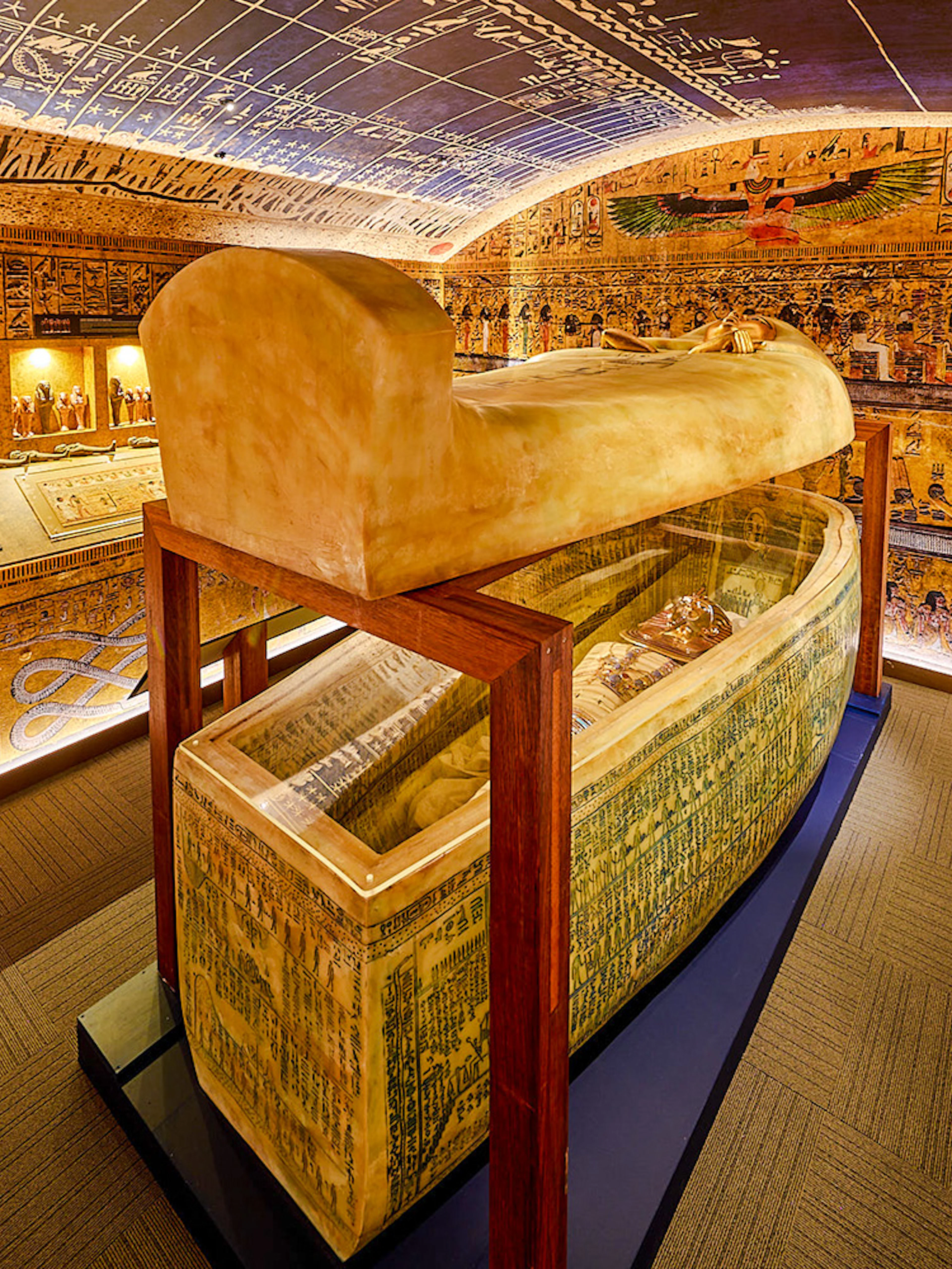 Open sarcophagus in a room with Egyptian paintings at the Tomb of the Pharaoh exhibit.