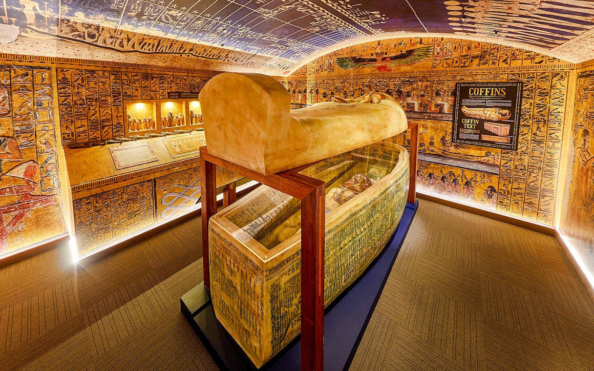 Open sarcophagus in a room with Egyptian paintings at the Tomb of the Pharaoh exhibit.