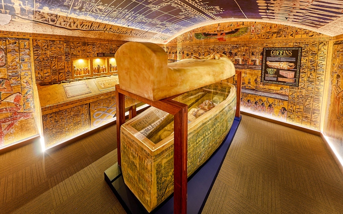 Open sarcophagus in a room with Egyptian paintings at the Tomb of the Pharaoh exhibit.