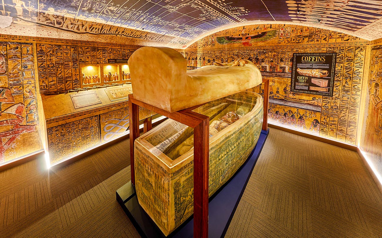 Open sarcophagus in a room with Egyptian paintings at the Tomb of the Pharaoh exhibit.