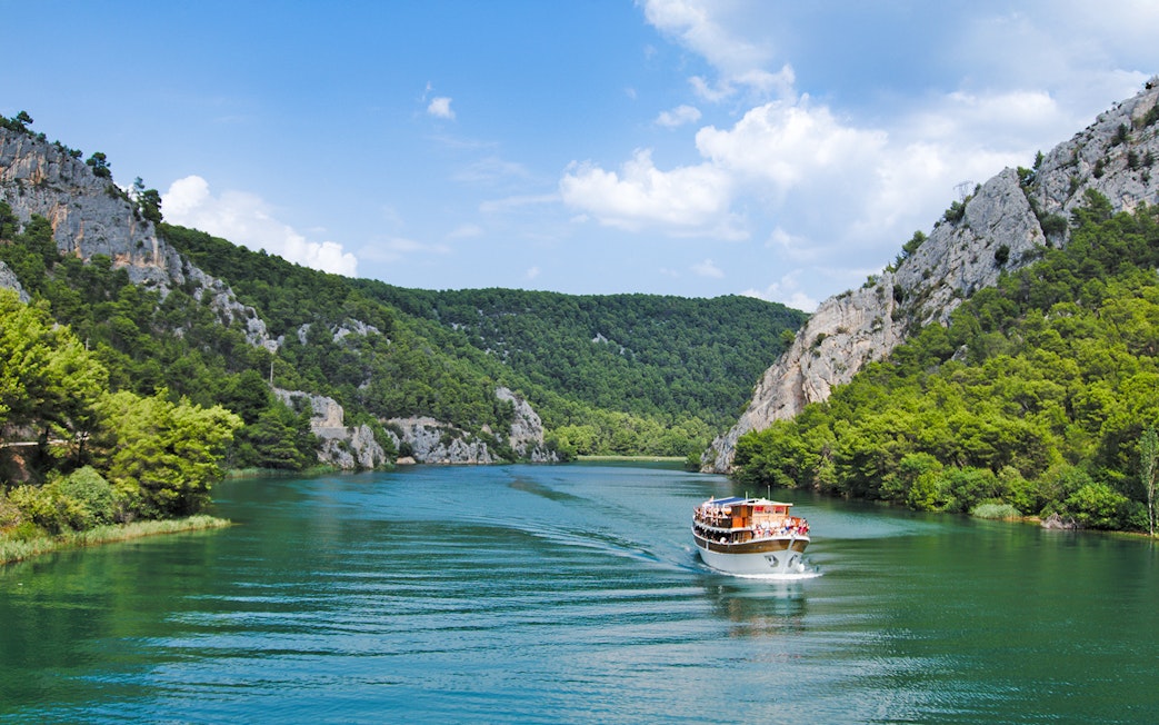 Boat cruising through Krka National Park's lush canyon, Croatia.