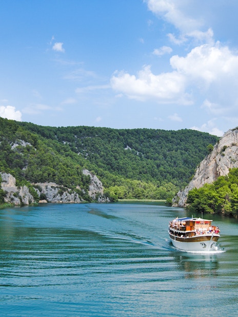 Boat cruising through Krka National Park's lush canyon, Croatia.